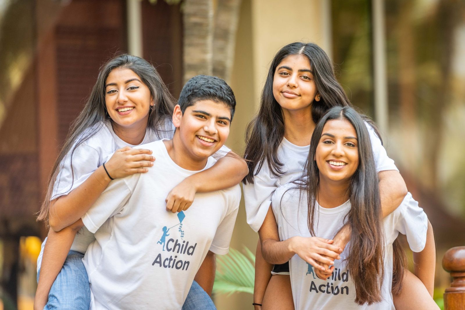 Four Child Action youth ambassadors in Child Action T-shirts, smiling and giving each other piggyback rides