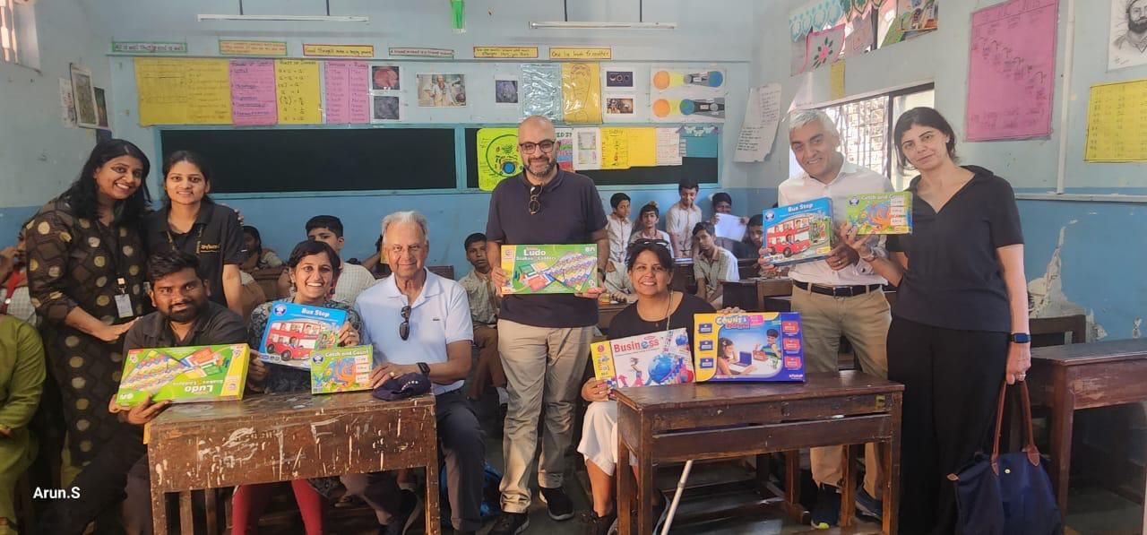 Seema, her family and Opentree staff holding board games in a Foundational Play classroom full of children