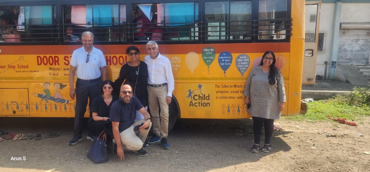 Seema and her family standing beside a Doorstep School on Wheels bus with children inside