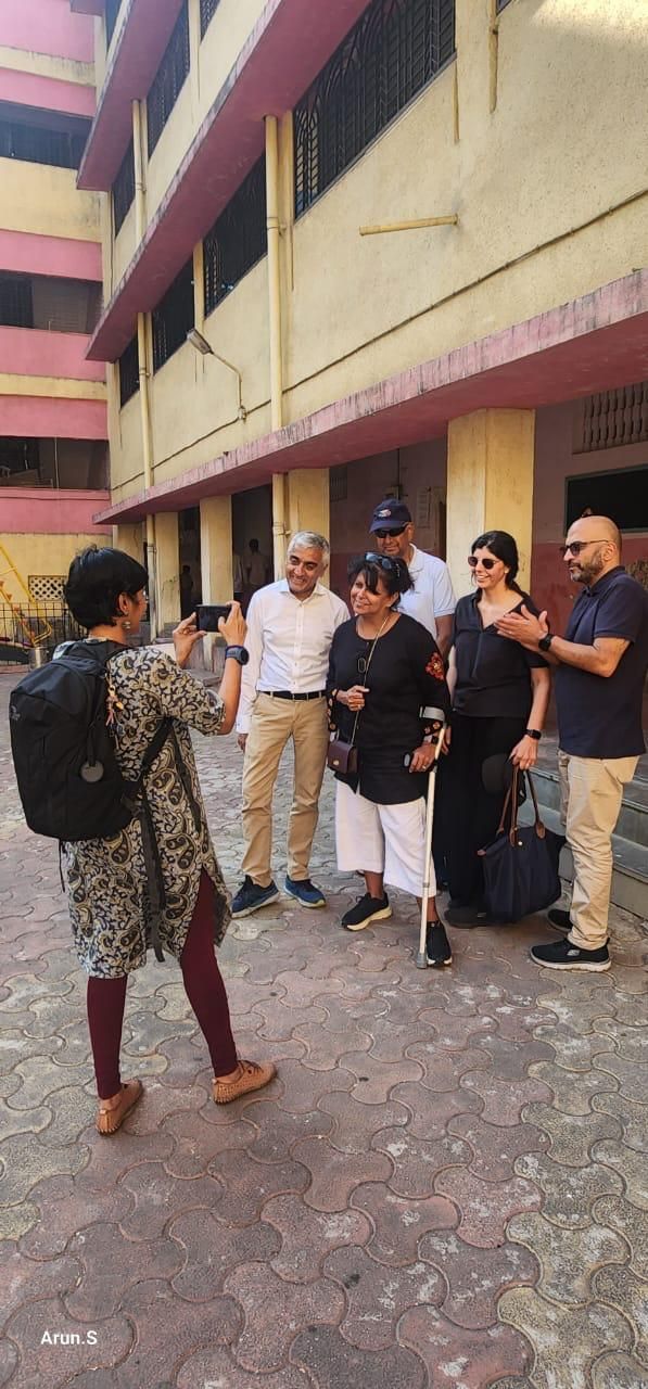 Seema, on crutches, with her family in a school courtyard in Mumbai while an Opentree team member takes their photo
