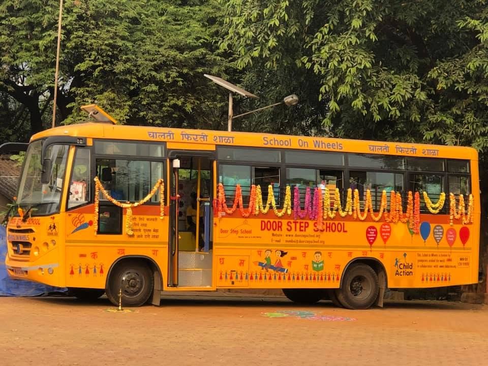 The bright yellow School on Wheels bus, decorated with flower garlands, with Door Step School and Child Action logos on its side